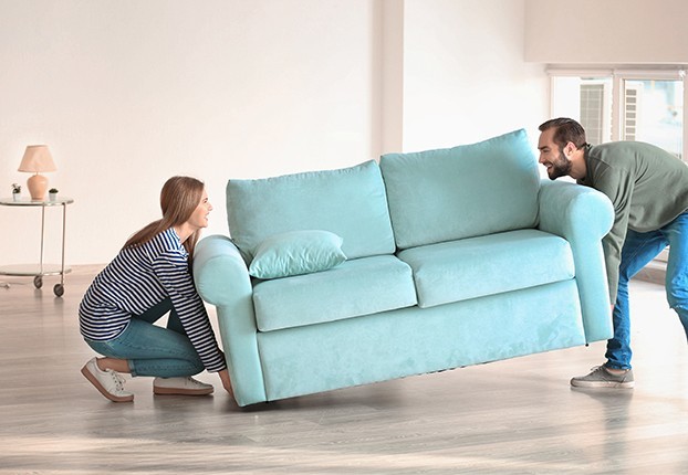 Young couple moving sofa in room at new home